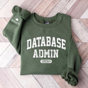 May include: A green sweatshirt with the text "DATABASE ADMIN EST 2024" in white. The sweatshirt has a crew neck and long sleeves.