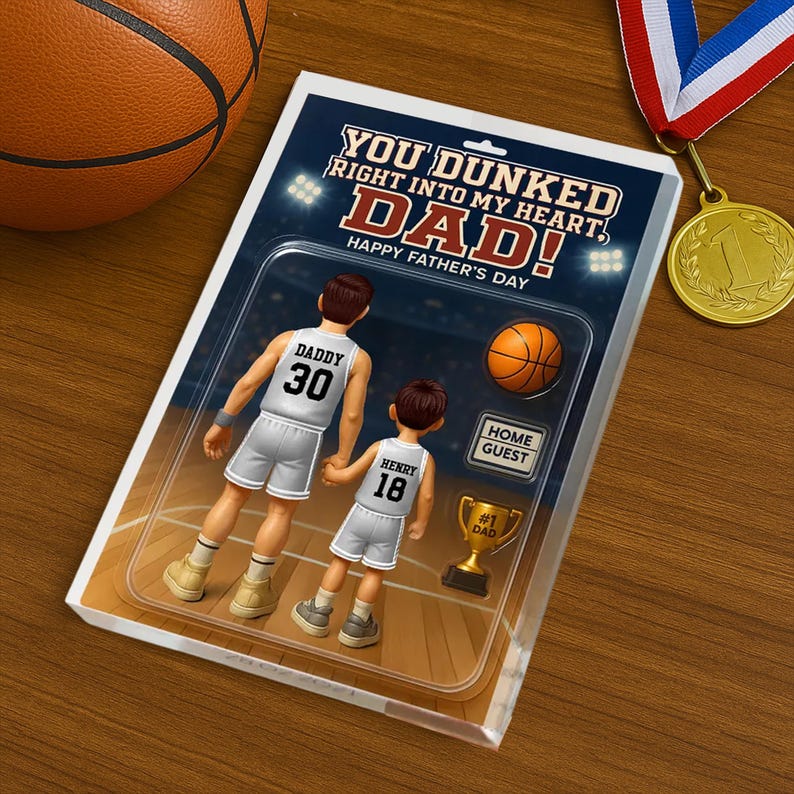 May include: A Father's Day card with a basketball theme. The card features a cartoon illustration of a father and son playing basketball. The text on the card reads "You dunked right into my heart, Dad! Happy Father's Day."