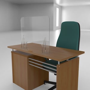 Puede incluir: Un protector de estornudos o partición de acrílico transparente sobre un escritorio de madera con una silla de oficina verde. El escritorio tiene un cajón y una barra de soporte de metal.