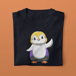 May include: Black t-shirt featuring a cartoon penguin wearing a purple and yellow striped shirt. The penguin has a yellow head and a white body.