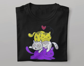 Op de afbeelding: Zwart T-shirt met een afbeelding van drie cartoonkatten die op elkaar gestapeld zijn. De onderste kat is paars, de middelste kat is grijs en de bovenste kat is geel. Een klein rood hartje bevindt zich boven de katten.