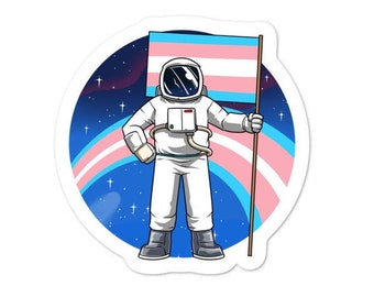 May include: A sticker depicting an astronaut in a white spacesuit, holding a flag with the transgender pride colours. The background shows a starry night sky and a rainbow-coloured arc.