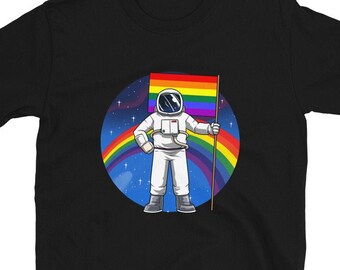 May include: Black t-shirt with a cartoon astronaut holding a rainbow flag. The astronaut is in a white spacesuit, set against a backdrop of a rainbow and a starry sky. The design celebrates LGBTQ+ pride.