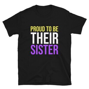 Puede incluir: Camiseta negra con el texto "Orgulloso de ser su hermana" en amarillo, blanco y morado.