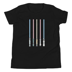Puede incluir: Camiseta negra con un diseño de cinco sables de luz en varios colores: azul claro, rosa, blanco y dos tonos de azul. Los sables de luz están alineados verticalmente y tienen empuñaduras detalladas.