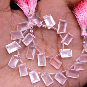 May include: A strand of rectangular, light pink rose quartz beads. The beads are strung together with a pink string and are accented with pink tassels at each end. The beads are translucent and have a polished finish.
