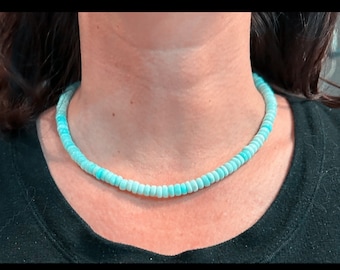 May include: A light blue beaded necklace made of small, round beads. The necklace is worn by a person, but the person's face is not visible.