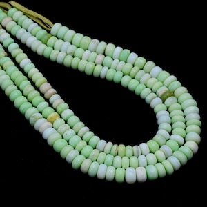 Könnte beinhalten: Eine Strähne aus hellgrünen Opalperlen mit einem leichten weißen Schimmer, auf einer dünnen Schnur aufgefädelt. Die Perlen sind rund und glatt und in einem lockeren, fließenden Muster angeordnet.