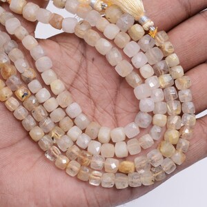 May include: A strand of faceted, golden rutilated quartz beads. The beads are a light yellow color with gold inclusions. The beads are strung on a string and are ready to be used for jewelry making.