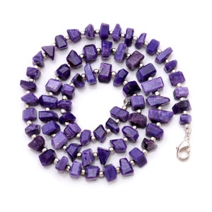 May include: A purple and silver necklace made of faceted gemstone beads. The necklace is made of a variety of shapes and sizes of beads, and it is strung on a silver chain.