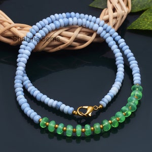 May include: A double-strand necklace made of light blue and green beads. The necklace has a gold clasp and is displayed on a woven surface.