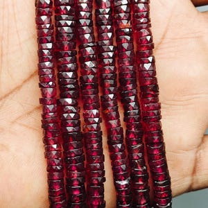 Op de afbeelding: Strengen gefacetteerde, dieprode edelstenen. De kralen zijn klein, rechthoekig en aan elkaar geregen, waardoor een ketting of armband ontstaat. De kleur is een rijk, donkerrood, met een lichte glans.