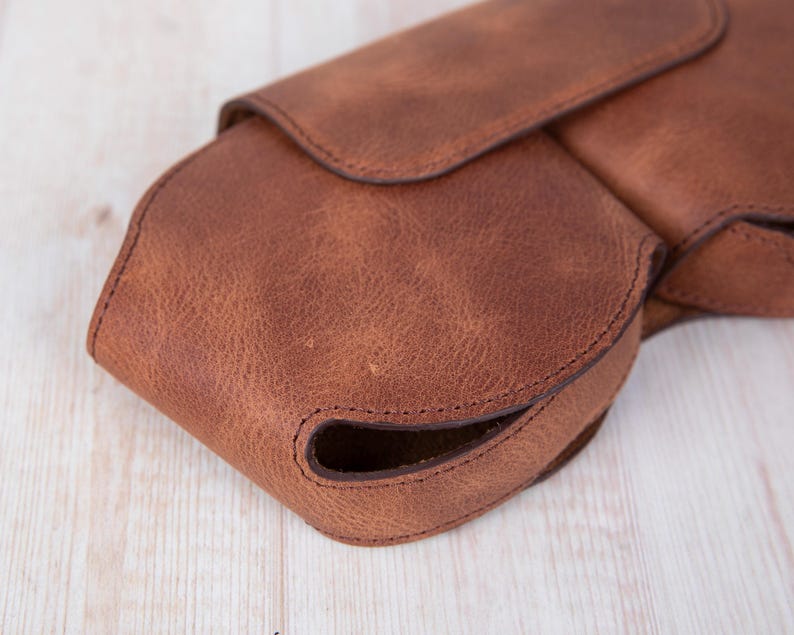 K&ouml;nnte beinhalten: Eine braune Ledertasche mit einem Klappverschluss und einem gen&auml;hten Design. Die Tasche hat eine abgerundete Form und eine glatte Textur.