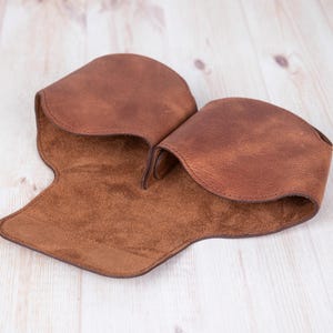 K&ouml;nnte beinhalten: Ein braunes Lederetui f&uuml;r Brillen mit einem Futter aus Wildleder. Das Etui ist ge&ouml;ffnet und das Futter ist sichtbar.