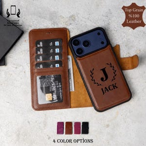 Könnte beinhalten: Eine braune Handyhülle im Brieftaschen-Stil aus Leder mit schwarzem Kameraausschnitt und einem personalisierten Design mit dem Buchstaben J und dem Namen JACK in einem Lorbeerkranz. Das Innere bietet mehrere Kartenfächer und ein Sichtfenster.