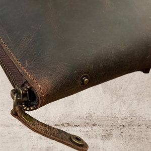 May include: A brown leather wallet with a zipper closure and a brown leather strap. The wallet has a distressed look and features brass accents.