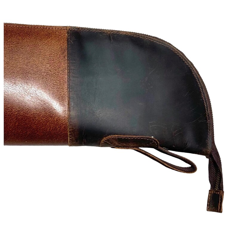 May include: A brown leather gun case with a zipper closure and a strap. The case has a dark brown leather flap with a stitched edge.