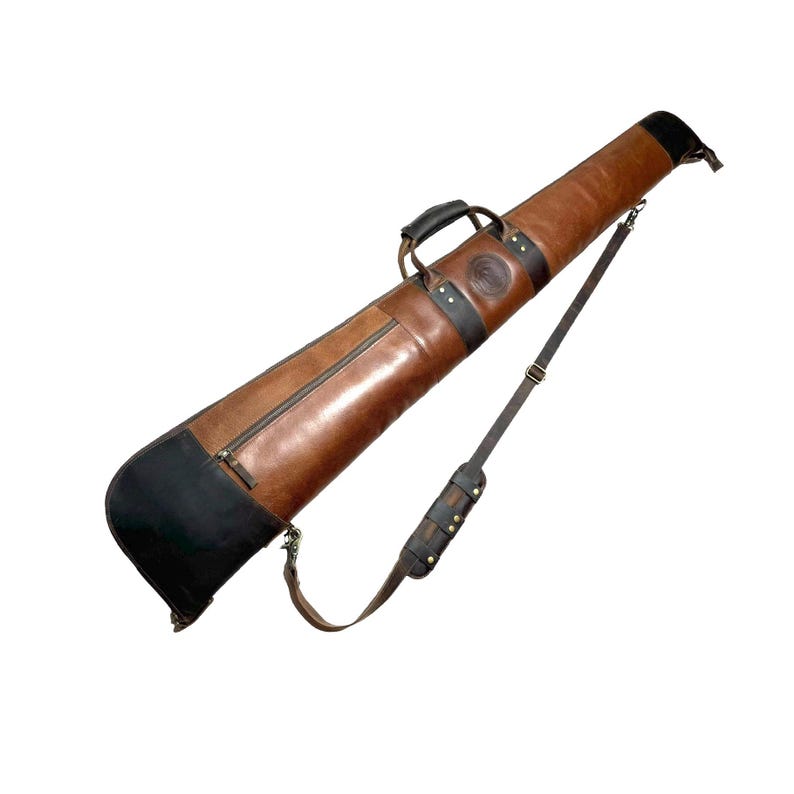 May include: A brown leather gun case with a black leather end cap and a shoulder strap. The case has a zipper closure and a handle.
