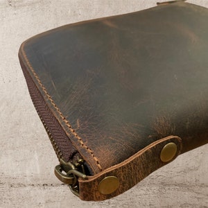 May include: A brown leather zippered pouch with two brass snaps and a zipper pull. The pouch has a distressed look and is made of a thick, durable leather.
