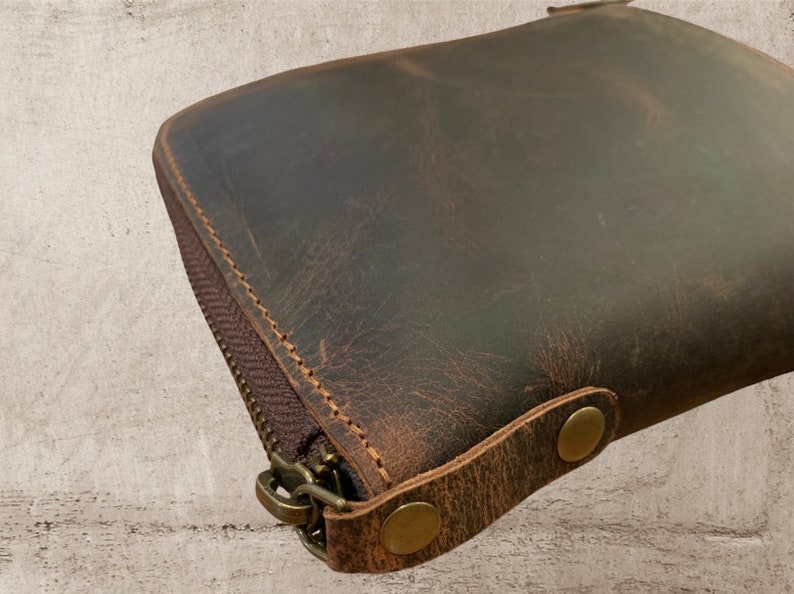 May include: A brown leather zippered pouch with two brass snaps and a zipper pull. The pouch has a distressed look and is made of a thick, durable leather.