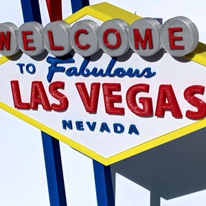 May include: A 3D-printed sign featuring the iconic "Welcome to Fabulous Las Vegas" design. The sign has a yellow border, white center, and red lettering. The word "Welcome" is on top, with "Las Vegas" below.