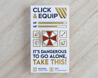 May include: Gold-coloured enamel pin featuring a red and white umbrella with a black symbol. The pin is on a white card with the text "CLICK & EQUIP" and "IT'S DANGEROUS TO GO ALONE, TAKE THIS!" in black and gold text.