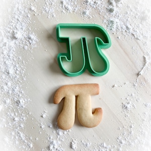 Könnte beinhalten: Ein grüner Plastik-Ausstecher in Form des mathematischen Symbols Pi und ein hellbrauner Keks, der in Form von Pi gebacken wurde.