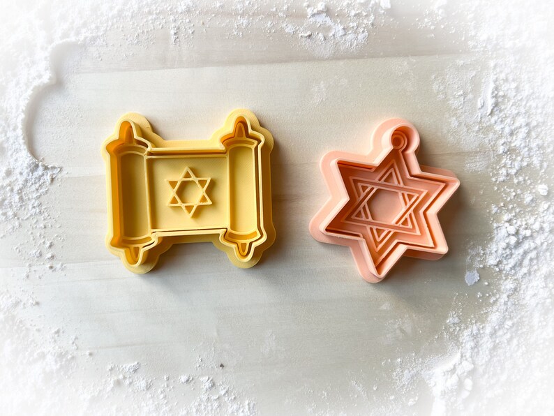 Op de afbeelding: Twee gele plastic koekjesvormen, een in de vorm van een Davidster en de andere in de vorm van een Thora-rol met een Davidster erin.
