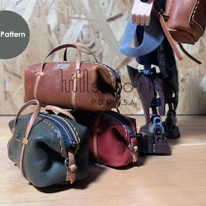 以下が含まれることがあります： 茶色、緑、赤のミニチュア革製のバッグ3つ。茶色のバッグには「JEEP」と印刷されています。バッグは積み重ねられています。