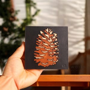 Puede incluir: Un recorte de piña marrón y naranja sobre un fondo negro. La piña es una silueta detallada con textura de veta de madera. El fondo es negro oscuro.