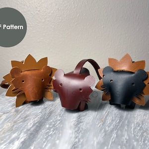 May include: Three leather lion keychains, one brown, one dark brown, and one black.  The keychains are all in the shape of a lion's head with a mane.  The keychains are on a light gray surface.  PDF Pattern.