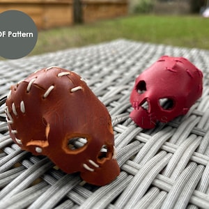 May include: Two leather skull keychains, one brown and one red, with white stitching. The keychains are on a woven wicker surface.  PDF Pattern.