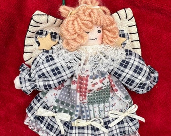 May include: A handmade fabric angel ornament with a plaid dress, a white lace collar, and a brown yarn wig. The angel has a green string hanger and a star on its wing.