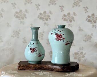 May include: Two ceramic vases with a light blue glaze and red floral designs. The vases are sitting on a wooden stand.