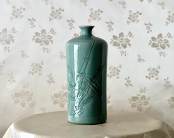 May include: A teal ceramic vase with a raised bamboo design. The vase has a rounded body and a narrow neck.