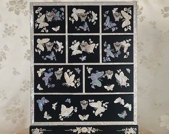 May include: A black wooden jewelry box with a decorative design of mother-of-pearl butterflies. The box has multiple drawers and is decorated with silver accents.