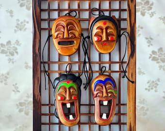 May include: Four traditional Korean masks hanging on a wooden frame. The masks are painted in bright colors and feature unique facial expressions. The frame is decorated with a lattice pattern.