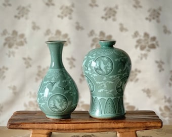 Può includere: Due vasi in ceramica verde celadon con finitura smaltata a crepa. Il vaso a sinistra ha un collo sottile e un corpo bulboso, mentre quello a destra è più largo con un collo corto. Entrambi presentano motivi di gru bianche intarsiate.