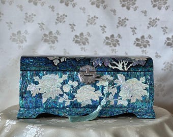 May include: A blue and white mother of pearl jewelry box with a floral design and a silver lock and keyhole. The box has a blue tassel.