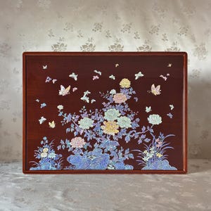 May include: A rectangular wooden tray with a dark reddish-brown finish. The tray is decorated with an inlaid floral design featuring peonies and butterflies in shades of white, yellow, pink, and blue. The tray has a simple, clean border.