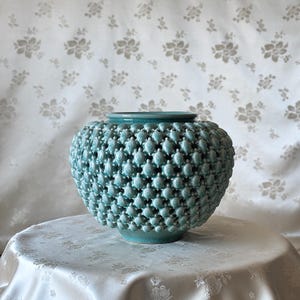 Pode incluir: Um vaso de cerâmica azul-turquesa com uma superfície texturizada que se assemelha a um grupo de pequenas protuberâncias arredondadas.