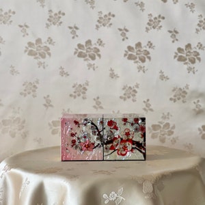 May include: A decorative box with a floral design. The box is made of wood and has a pink and white finish. The floral design features pink and red flowers and green leaves.