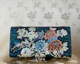 May include: A dark blue clutch purse with a floral design made of iridescent mother of pearl. The flowers are in shades of pink, blue, and white. The purse has a silver clasp.