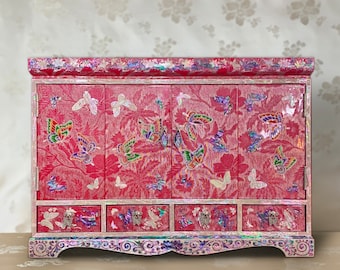 May include: A red wooden cabinet with four doors and three drawers. The cabinet is decorated with a butterfly motif and iridescent mother-of-pearl inlay.