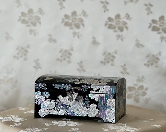 Pode incluir: Uma caixa de madeira preta com tampa articulada, decorada com um desenho floral de madrepérola iridescente. A caixa tem um detalhe de borboleta prateada na tampa.