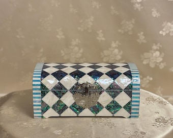 May include: A small, rectangular, decorative box with a checkered pattern in black, white, and iridescent blue. The box has a hinged lid with a silver latch.