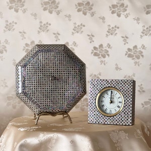 May include: Two decorative items made of mother of pearl with a geometric pattern. The first item is an octagonal box with a stand. The second item is a square clock with Roman numerals.