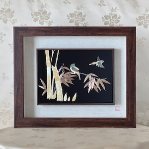 May include: A framed artwork featuring two birds perched on bamboo branches. The birds are crafted from natural materials, such as feathers and leaves, and are displayed against a black background. The frame is brown wood with a white mount.