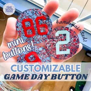 May include: Hand-painted mini buttons with red and blue splatter paint and white numbers. The buttons say "mini buttons!" and "hand painted!"  "CUSTOMIZABLE GAME DAY BUTTON"