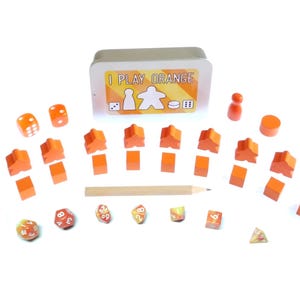 Peut inclure: Des pièces de jeu orange, des dés et une boîte en métal avec le texte "I Play Orange" sur le devant. Les pièces de jeu sont en forme de personnes et sont en bois. Les dés sont numérotés de 1 à 6. La boîte en métal est orange et blanche.